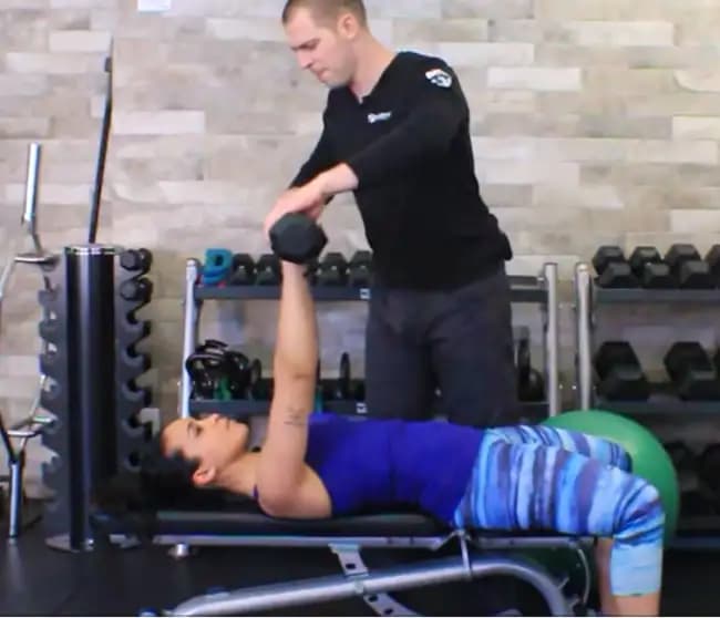 Dr. Brent Brookbush cues Melissa through multi-planer dumbbell press on bench