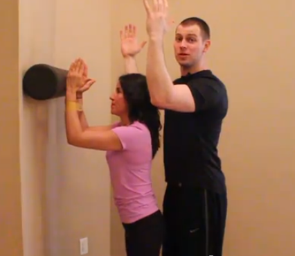Dr. Brookbush teaches a client serratus anterior activation with a foam roll to aid in this modification of a wall slide, and with a band around forearms to resist external rotation.